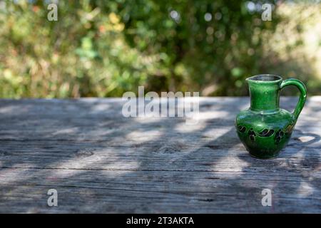 Leerer Tisch aus verwitterten Holzplatten, mit grüner Keramikvase, seitlicher Blick auf leere Kulisse Stockfoto