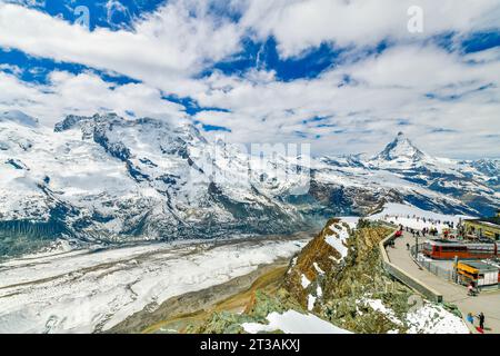 Roter Zug auf verschneite Bahn an Gipfelstation mit Touristen und Matterhorngipfel und Gorner Gletscher in der Schweiz Stockfoto