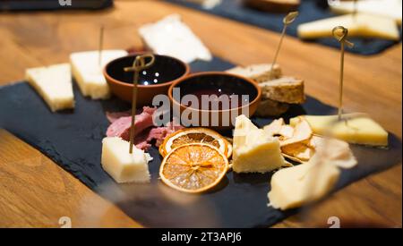 Gourmet-Wurstkeramik-Steinplatte mit verschiedenen Käsesorten, getrockneten Früchten, Erdbeeren, Birnen, geschnittenem Brot, Räucherfleisch, würzige Dip-Marmeladen-Soßen auf r Stockfoto