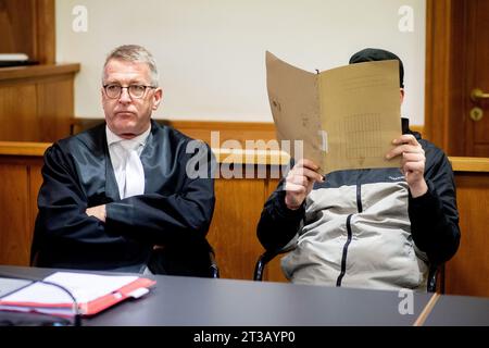 Oldenburg, Deutschland. Oktober 2023. Der Angeklagte (r) sitzt neben seinem Anwalt Andreas Lauven in einem Gerichtssaal vor dem Amtsgericht und hält einen Aktenschutz vor seinem Gesicht. Der Untersuchung zufolge soll der Mann im April 2023 in einer Klinik in Bad Zwischenahn mit massiver Gewalt gegen den Hals einen weiteren Patienten getötet haben. Während des Prozesses leugnete der Angeklagte das Verbrechen. Quelle: Hauke-Christian Dittrich/dpa/Alamy Live News Stockfoto