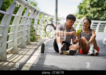 Junges asiatisches Paar teilt Handyfotos während einer Pause während des Trainings im Freien Stockfoto