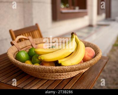 Frische Bananen in einem Korb mit verschiedenen Früchten auf einem hölzernen Gartentisch. Stockfoto
