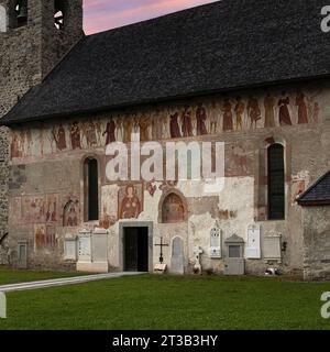 Südfassade der Chiesa di San Vigil (Kirche St. Vigil oder Kirche St. Vigil von Trient) in Pinzolo, Trentino-Südtirol, Italien. Entlang der Mauer, unterhalb der Traufe, befindet sich ein Freskenfries Tanz des Todes, gemalt 1539 von Simone II. Baschenis (ca. 1495–1555). Links beginnt die Friesprozession: Eine gekrönte Todesfigur spielt den Dudelsack, begleitet von zwei weiteren Skeletten, die Hörner spielen; ihnen folgt Christus am Kreuz, dann 18 Menschen mit sehr unterschiedlichen Positionen in der Gesellschaft, jeder durchbohrt vom Pfeil des Todes, mit lächelnden Skeletten. Stockfoto