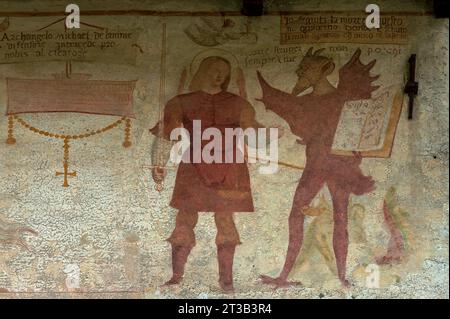 Detail aus dem 16. Jahrhundert Danza Macabra (Tanz des Todes) Freskenfries: Erzengel Saint Michael hält ein Schwert und der Teufel hält ein Buch, auf dem die sieben tödlichen Sünden geschrieben sind. Gemalt von der italienischen Künstlerin Simone II. Baschenis (ca. 1495–1555) an der Außenwand der Chiesa di San Vigil in Pinzolo, Trentino-Südtirol, Italien. Stockfoto