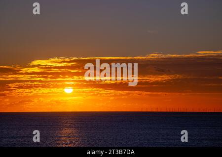 Sonnenuntergang über dem Ärmelkanal im Dezember, mit Rampion Wind Farm Turbinen am Horizont und sonnendurchflutetem Pfad auf dem Meer. Stockfoto