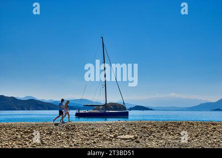 Segelyacht vor Anker im Golf von Fethiye, im Süden der Türkei mit einem Paar am Strand und Blick auf die Berge. Stockfoto