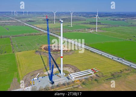 Aus der Vogelperspektive über die Baustelle mit Rotorblättern auf dem Boden und Baukran zur Montage von Stahlturmabschnitten der Windkraftanlage im Windpark Stockfoto