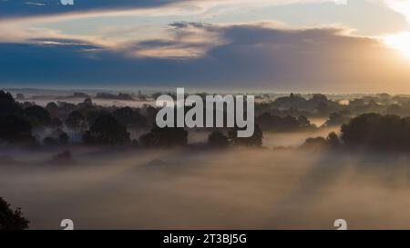 Am frühen Morgen kriecht Nebel oder Nebel über die Felder und Wälder in der Nähe von Emsworth in Hampshire. Heller Sonnenschein, der die Szene und lange Schatten beleuchtet. Stockfoto