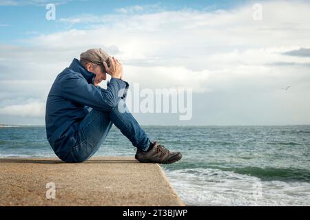 Mann, der am Meer sitzt, mit dem Kopf in den Händen, Emotionen, geistiges Gesundheitskonzept Stockfoto