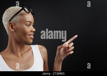 Black Friday Shopping. Profilporträt lächelnd einer schwarzen Frau mit einer Brille auf dem Kopf, die Finger auf schwarzem Hintergrund mit Kopierraum zeigt. Anzeige Stockfoto