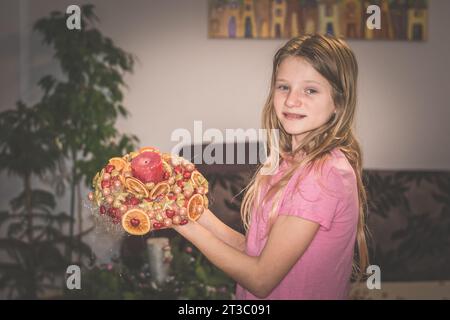 Niedliches Mädchen, das einen weihnachtskranz mit Kugeln und anderen bunten Glitzerdekorationen kreiert Stockfoto