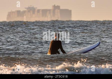 Isle Of Palms, Usa. Oktober 2023. A Suder beobachtet ein riesiges Containerschiff vor der Küste, während es am 24. Oktober 2023 auf der Isle of Palms in South Carolina auf eine Welle wartet. Quelle: Richard Ellis/Richard Ellis/Alamy Live News Stockfoto