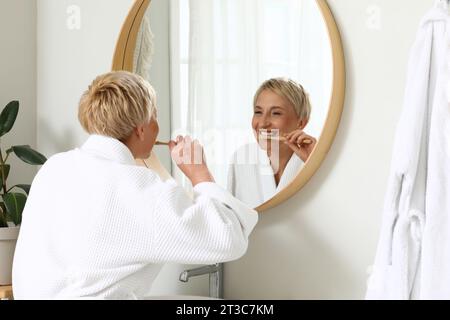 Reife Frau, die Zähne in der Nähe des Spiegels im Badezimmer putzt Stockfoto