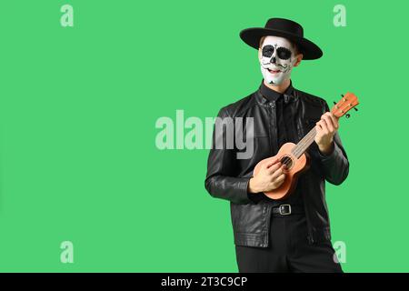 Junger Mann mit bemaltem Schädel, der Gitarre auf grünem Hintergrund spielt. Mexikanischer Tag der Toten (El Dia de Muertos) Stockfoto