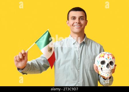Schöner junger Mann mit bemaltem Schädel und mexikanischer Flagge auf gelbem Hintergrund Stockfoto