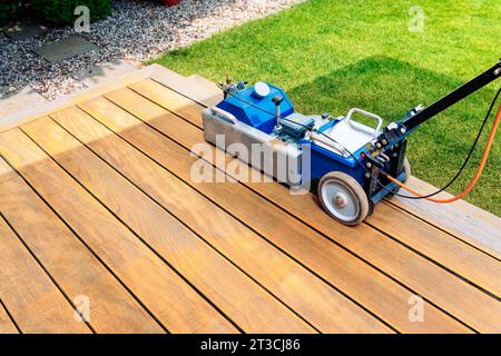 Maschinenreinigung einer Holzterrasse - Trockenmethode - Schleifen der Bretter mit Schleifmaschine, Vorbereitung zum Ölen der Terrasse Stockfoto