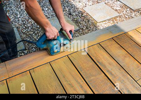 Maschinenreinigung einer Holzterrasse - Trockenmethode - Schleifen der Bretter mit einer praktischen Schleifmaschine, Vorbereitung zum Ölen der Terrasse Stockfoto