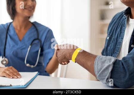 Arzt schüttelt die Hände mit männlichem Patienten, der während des Arzttermins ein Krankenarmband trägt Stockfoto