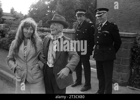 Ein älterer Zigeuner mit Trilby-Hut und einem traditionell gebundenen Halstuch mit einer jungen Frau am Arm. Er ist Henry Gaskin, er war im Bierzelt und hatte ein paar zu viele. Er singt jedem ein Lied. Sie sieht etwas peinlich aus und zwei Polizeichefs sehen amüsiert aus. Appleby in Westmorland Gypsy Horse Fair Cumbria, England Juni 1981 1980S UK HOMER SYKES Stockfoto