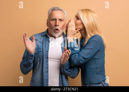 Reife Frau, die ihr Geheimnis mit ihrem Mann teilt, beigefarbener Hintergrund Stockfoto