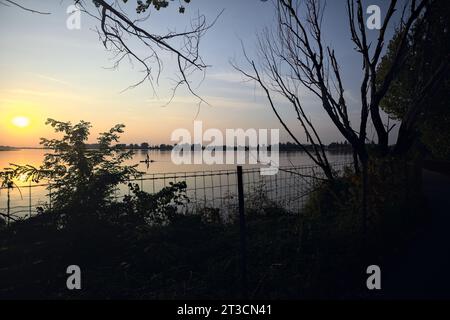 Mann auf einem Floß über einem See bei Sonnenuntergang, eingerahmt von Bäumen Stockfoto