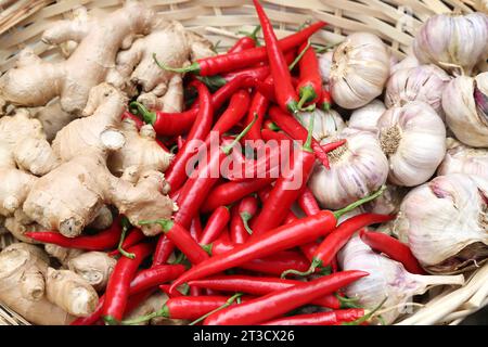 Ein gewebter Korb gefüllt mit Ingwer, roter Chilischote und Knoblauch. Der Ingwer ist hellbraun und in großen Stücken. Die roten Chilis sind hellrot. Die Stockfoto