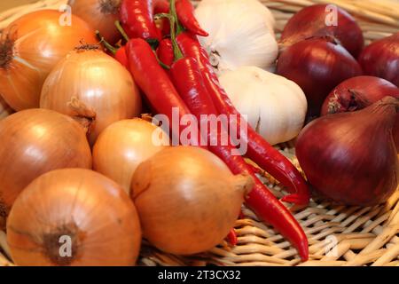 Ein gewebter Korb gefüllt mit roten Chilischoten, weißem Knoblauch und gelben Zwiebeln. Der Korb besteht aus gewebtem Stroh. Die Chilischoten sind lang und Stockfoto