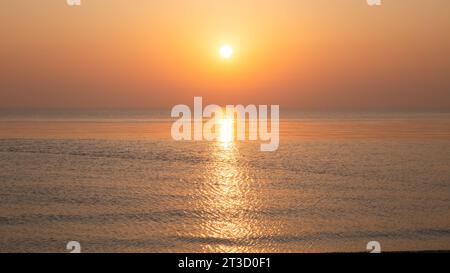 Orange Meer Sonnenuntergang mit Wellen und Schnee/Eis am Meer Stockfoto