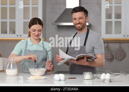 Glückliches Paar, das Rezept im Kochmagazin liest, während er zu Hause kocht Stockfoto