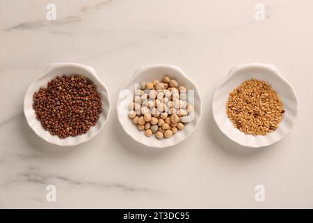 Microgreens anbauen. Verschiedene Samen in Schüsseln auf weißem Marmortisch, flach gelegt Stockfoto