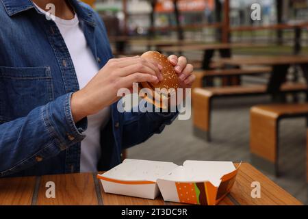 Lemberg, Ukraine - 9. Oktober 2023: Frau mit McDonald's Burger am Holztisch im Freien, Nahaufnahme Stockfoto