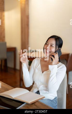 Eine fröhliche und schöne asiatische Frau spricht gern mit ihrem Freund am Telefon, während sie sich in einem Café entspannt. Lifestyle, Menschen und Technologie Stockfoto