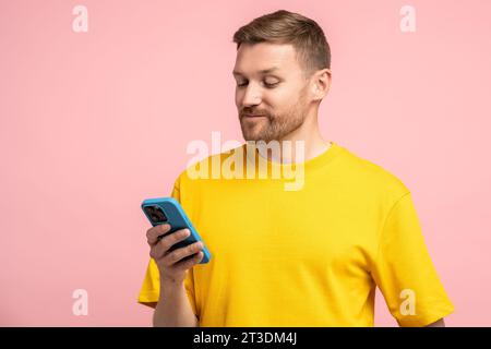 Bärtiger Mann, der auf den Bildschirm des Mobiltelefons blickt, mit zufriedenem Gesicht zufrieden mit guten Nachrichten, Nachricht Stockfoto