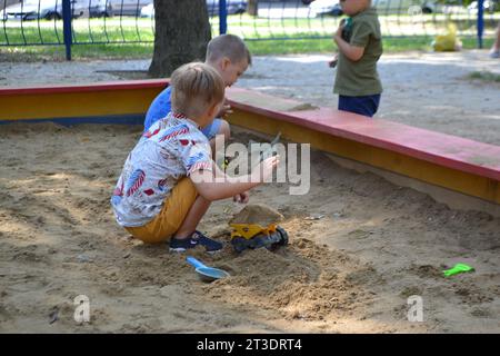 Niedlicher Kleinkinder, der im Sand auf dem Spielplatz im Freien spielt. Wunderschönes Baby, das Spaß an sonnigen warmen Sommertagen hat. Hochwertige Fotos Stockfoto