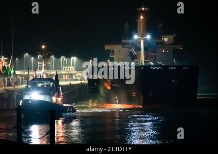 Cuxhaven, Deutschland. Oktober 2023. Das Frachtschiff „Polesie“ wird nachts von zwei Schleppbooten an den Kai der Seebad-Brücke gezogen. Nach dem Zusammenstoß zweier Frachter in der Nordsee vor Helgoland wurden die vier vermissten Personen der siebenköpfigen Besatzung noch nicht gefunden. Quelle: Jonas Walzberg/dpa/Alamy Live News Stockfoto