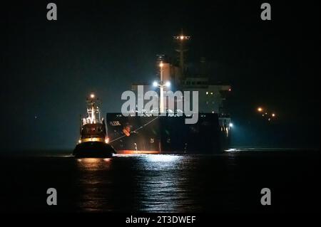 Cuxhaven, Deutschland. Oktober 2023. Das Frachtschiff Polesie wird nachts von zwei Schleppern in der Elbmündung nach Cuxhaven geführt. Nach dem Zusammenstoß zweier Frachter in der Nordsee vor Helgoland wurden die vier vermissten Personen der siebenköpfigen Besatzung noch nicht gefunden. Quelle: Jonas Walzberg/dpa/Alamy Live News Stockfoto