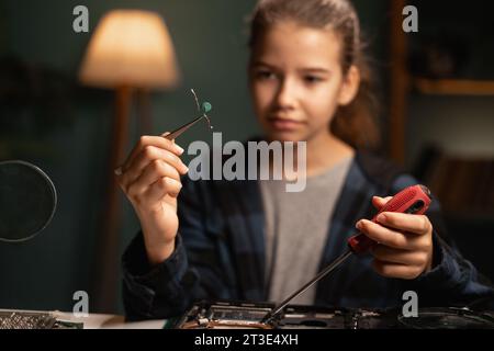 Computer-Reparaturwerkstatt für Kinder. Intelligentes Schulmädchen für die Wartung von Notebooks. Kinder-DIY-Befestigung von elektronischen Bauteilen. Stockfoto