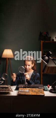 Hobby für einen Teenager. Ein Teenager-Mädchen, das zu Hause einen Laptop repariert, verwendet eine Lupe und interessiert sich für Elektronik. Intelligentes Kind im Stockfoto