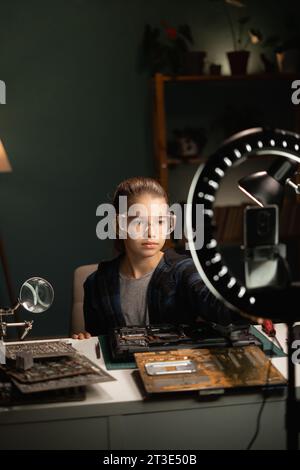 Teen Girl macht Videoinhalte für soziale Medien mit Smartphone und Ringlampe. Blogger, der über die Reparatur von Laptops auf dem Smartphone-Bildschirm spricht. Macht Stockfoto