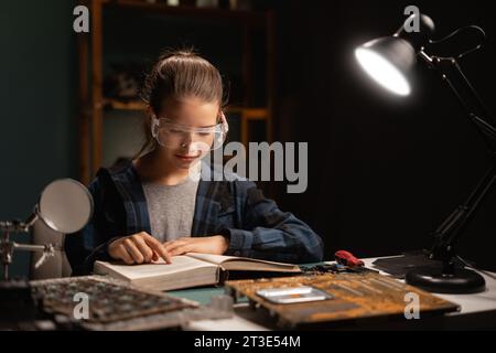 Teenager Mädchen zur freien Verfügung am Schreibtisch lernt Löten, Mädchen hat eine Schutzbrille, liest Bücher und repariert Kabel, Elektronik Stockfoto