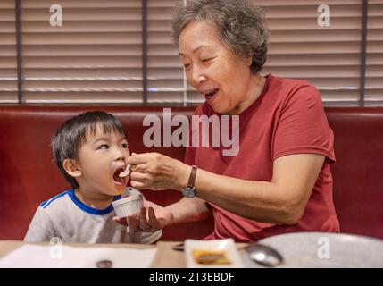 Glückliche Großmutter füttert ihren Enkel im Restaurant Stockfoto