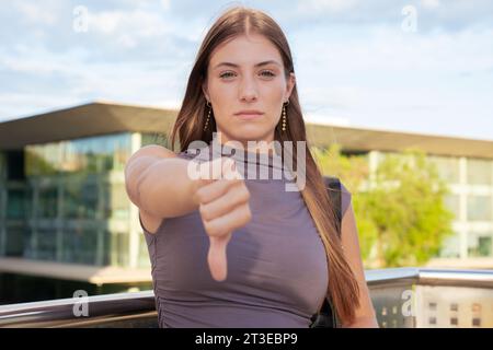 Porträt Junge wütende kaukasische Frau, die den Daumen nach unten zeigt und im Freien nachdenklich aussieht. Stockfoto