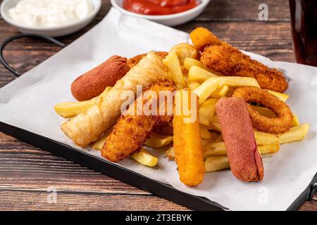 Snackteller mit Pommes frites, knusprigem Huhn, Käsestäbchen, Wurst und Frühlingsrollen auf Holztisch Stockfoto