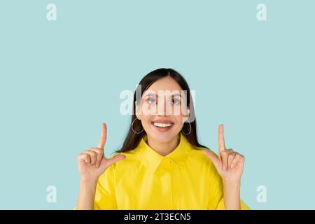 Fröhliche junge Frau, die auf den Kopierraum oben zeigt Stockfoto