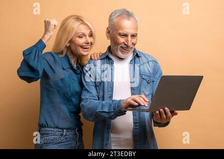 Emotionales Seniorenpaar mit Laptop auf beigefarbenem Hintergrund Stockfoto