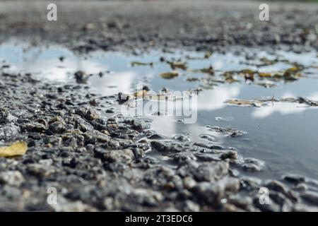 Pfützen mit Himmelsreflektion auf Schotterpiste Stockfoto