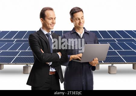 Geschäftsmann und Fabrikarbeiter, die einen Laptop vor Solarpaneelen auf weißem Hintergrund betrachten Stockfoto