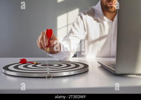 Geschäftsmann, der am Schreibtisch im Büro einen Pfeil auf das Ziel hält, um ein erfolgreiches Ziel zu erreichen. Stockfoto