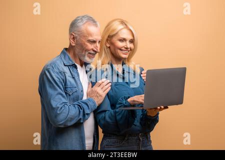 Glückliches Seniorenpaar mit Laptop, beigefarbener Hintergrund Stockfoto