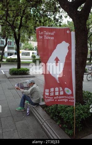 *** STRENG KEIN VERKAUF AN FRANZÖSISCHE MEDIEN ODER VERLAGE - RECHTE VORBEHALTEN ***08. Oktober 2023 - Taipeh, Taiwan: Ein Mann liest eine Zeitung in der Nähe einer großen Kampagne Flaggen zur Unterstützung der Unabhängigkeit Taiwans im Bezirk Ximending. Die Flaggen wurden von einer kleinen Gruppe namens "Taiwan Independence Flag Team" gesetzt, die sich für ein Referendum zur Selbstbestimmung einsetzt. Dieses Bild war Teenager am 1. Oktober, dem Nationaltag der Volksrepublik China. Stockfoto